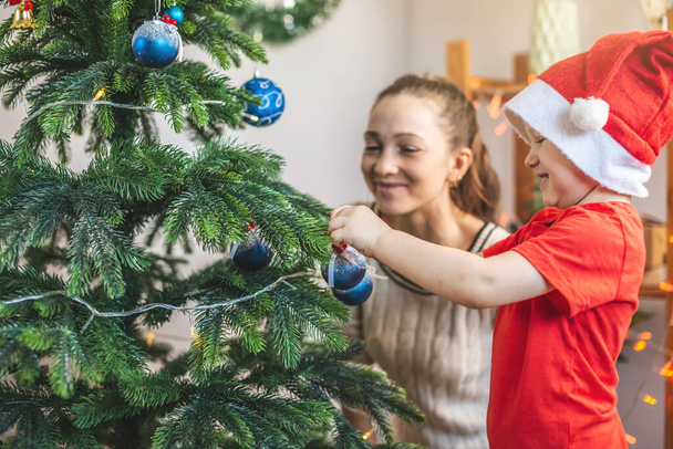Mother with her child son is decorating the Christmas tree with toys and Christmas balls. Happy family time on new year's eve at home - Foto, immagini