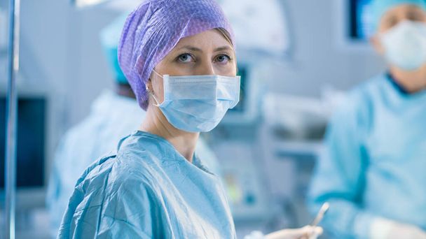 Πορτρέτο ενός νοσοκόμου κοιτάζοντας κάμερα κατά τη διάρκεια της λειτουργίας στο χειρουργείο. Επαγγελματίες γιατροί Εκτελώντας Χειρουργική. - Φωτογραφία, εικόνα