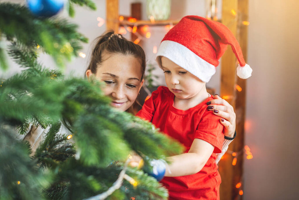 Mother with her child son is decorating the Christmas tree with toys and Christmas balls. Concept of a happy loving family on new year's eve - Foto, immagini
