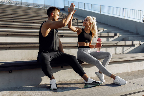 Sportive young couple, sitting on stairs outdoors and giving each other high five, fitness people after successful workout - Photo, image