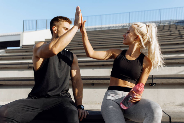 Sportive young couple, sitting on stairs outdoors and giving each other high five, fitness people after successful workout - Foto, afbeelding