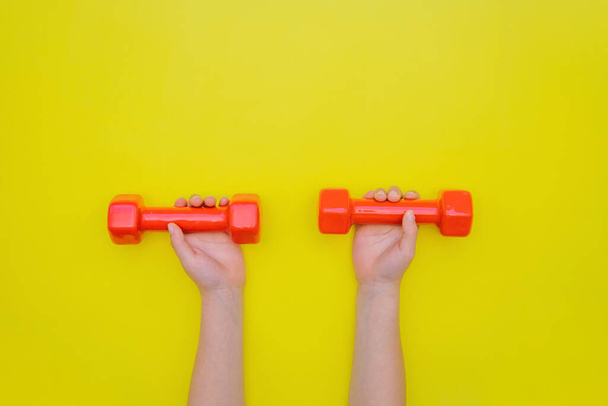 Childrens hands hold red dumbbells on a yellow background. - Foto, immagini