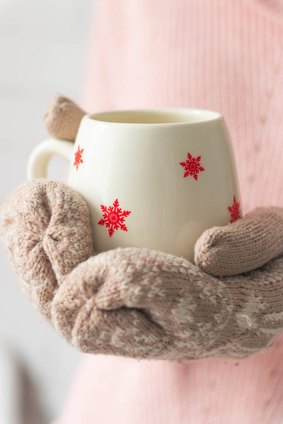 Fille tenant tasse avec des flocons de neige près sur fond clair.Fille mains en gants de sarcelle tenant une tasse avec du cacao chaud, thé ou café. Concept d'hiver et de Noël. - Photo, image