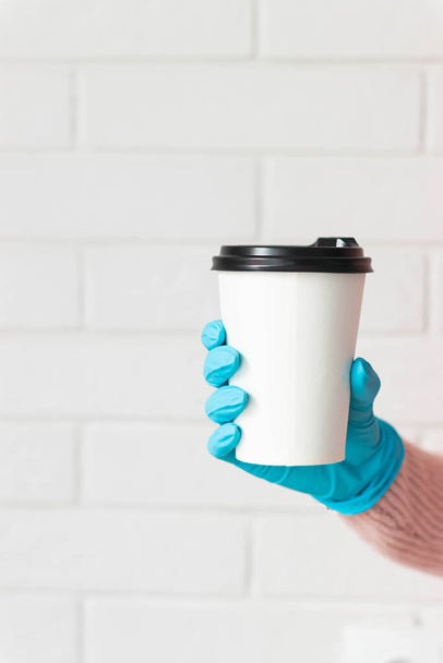 Girl holding white paper cup of takeaway coffee in the medical gloves. Place for your text or log. Coffee to go in holder. - Fotó, kép
