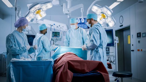 Diverse Team of Professional Surgeons Performing Invasive Surgery on a Patient in the Hospital Operating Room. Nurse Hands Out Instruments to surgeon, Anesthesiologist Monitors Vitals. Modern Hospital - Photo, image