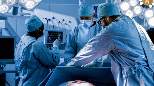 Diverse Team of Professional Surgeons Performing Invasive Surgery on a Patient in the Hospital Operating Room. Nurse Hands Out Instruments to surgeon, Anesthesiologist Monitors Vitals. Cold and Blue - Foto, imagen