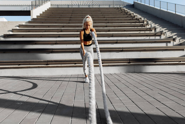 Sporty young woman, doing crossfit exercises with fighting ropes, outdoors in the city, ropes, sports, motivation - Foto, immagini