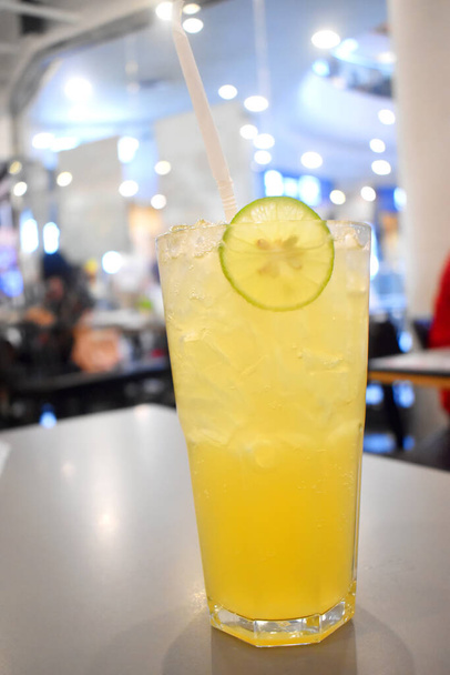 Zumo de limón mixto de miel con hielo en vaso con paja para beber negra en la mesa con fondo borroso en el restaurante - Foto, imagen