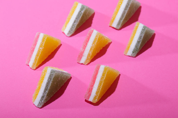 Conjunto de coloridos caramelos triangulares de gelatina alineados sobre fondo rosa. - Foto, Imagen
