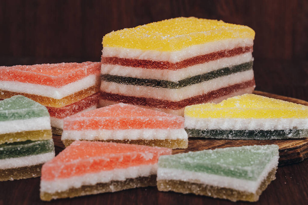 Разноцветные конфеты с мармеладом. Куча треугольных и прямоугольных конфет из мармелада, покрытых сахаром на деревянном фоне. - Фото, изображение