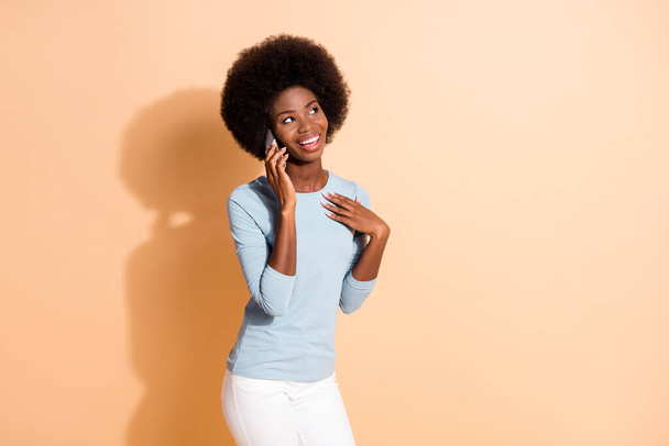 Фотографічний портрет красивої темношкірої дівчини, що розмовляє на мобільному телефоні, посміхаючись, дивлячись ізольовано на бежевому кольоровому фоні
 - Фото, зображення