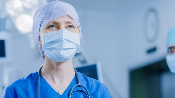 Portrait of the Professional Nurse Medical Assistant in Surgical Mask after Successful Operation. In the Background Modern Hospital Operating Room. - Foto, Imagen