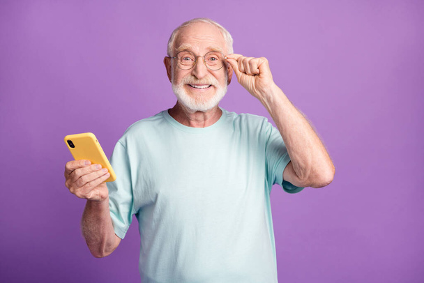 Photo portrait of happy man touching glasses holding phone in one hand isolated on vivid violet colored background - Fotó, kép