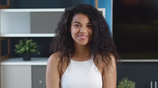 Portrait of beautiful stylish african american young woman smiling at camera on home interior background. Black fashion model with curly hair smiling for the camera at living room. - Footage, Video