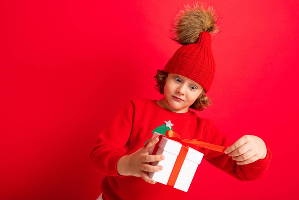 curly blond boy with a gift in his hands on a red background - Φωτογραφία, εικόνα