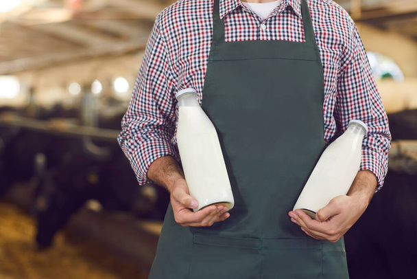 Farmer showing bottles of fresh natural cow milk and yoghurt manufactured on his farm - 写真・画像