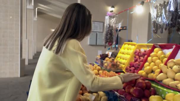 Mulher de casaco amarelo escolhe uma fruta fresca no mercado - Filmagem, Vídeo