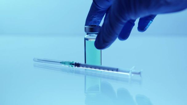 Vaccine against COVID-19 concept. Lab scientist holding sterile vial with blue antivirus. Searching for a cure from respiratory syndrome strain of coronavirus. World race in researching depiction. - Foto, imagen