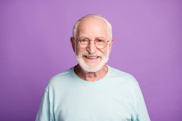 Portrait of smiling optimistic beard pensioner man wear light blue t-shirt eyeglasses isolated on purple color background - Photo, Image