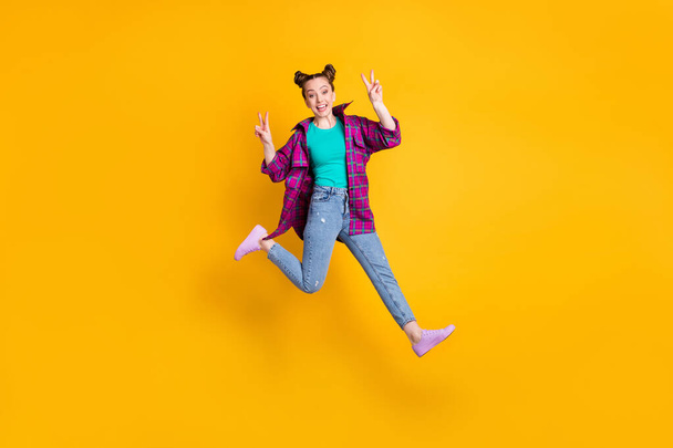 Full size photo of attractive lady jump show v-sign symbols greet friends meeting after self isolation wear casual plaid magenta shirt jeans sneakers isolated yellow vivid color background - Foto, afbeelding