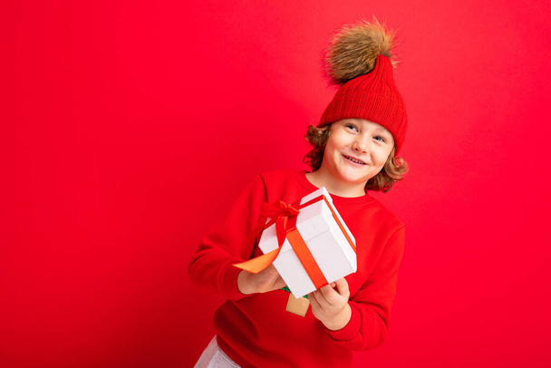 krullend blond jongen met een geschenk in zijn handen op een rode achtergrond - Foto, afbeelding