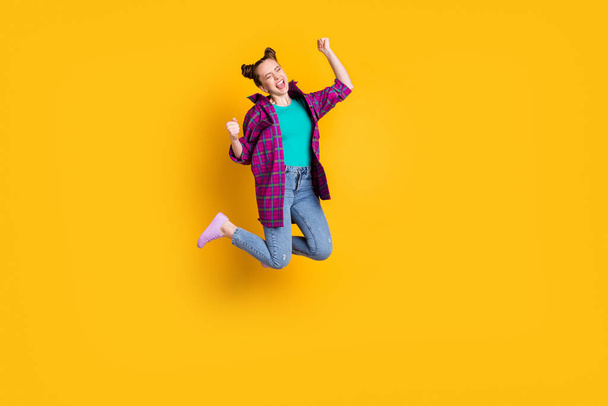 Full length photo of attractive crazy excited teen lady jump up air support sports team raise fists scream goal cheering wear casual plaid shirt shoes jeans isolated yellow color background - Foto, afbeelding