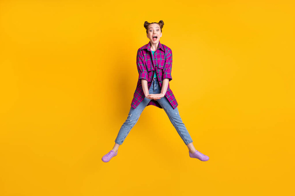 Full size photo of pretty funky crazy excited teen lady jump up good mood rejoicing spread legs summer weekend wear casual plaid shirt sneakers jeans isolated yellow color background - Foto, immagini