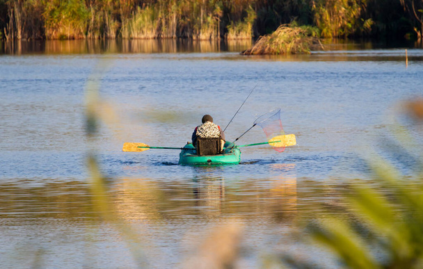 Am frühen Morgen sitzt ein Fischer in einem Boot in der Mitte des Sees und fängt Fische - Foto, Bild