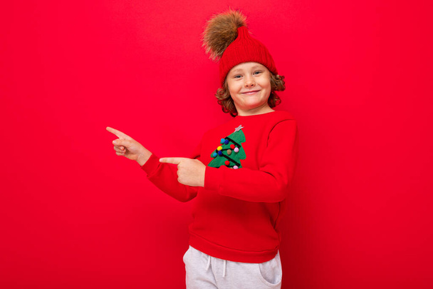 cool boy with curls on a red background in a sweater with a christmas tree - Φωτογραφία, εικόνα