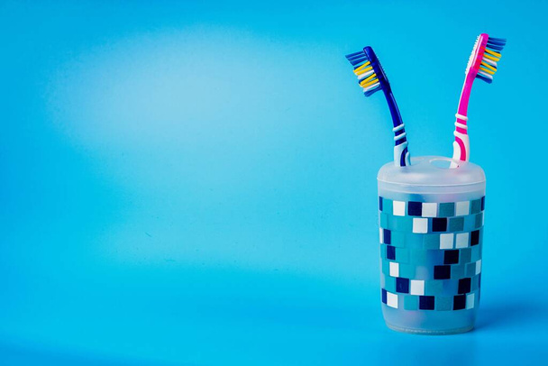 Πολύχρωμες οδοντόβουρτσες σε πλαστικό κύπελλο που απομονώνονται σε μπλε φόντο. Έννοια στοματικής υγιεινής και φροντίδας - Φωτογραφία, εικόνα