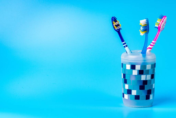 Wielokolorowe szczoteczki do zębów w plastikowym kubku izolowanym na niebieskim tle. Koncepcja higieny jamy ustnej i opieki - Zdjęcie, obraz
