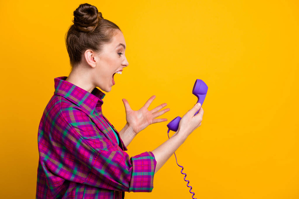 Profile photo of crazy angry furious lady two funny buns yell into cable telephone handset line bad connection cant speak boyfriend wear casual plaid shirt isolated yellow color background - Photo, Image