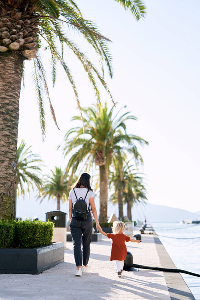 Madre e figlia stanno facendo una passeggiata vicino alle palme in un porto turistico in Montenegro - Foto, immagini