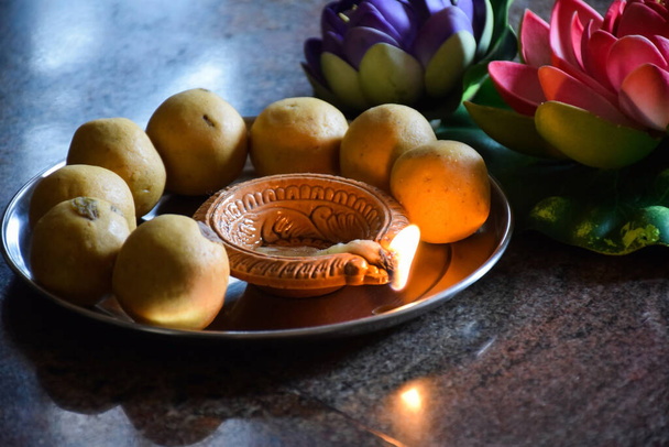 Besan laddo compuesto de harina de gramo y jarabe de azúcar decorado en la placa de acero y lámpara de aceite encendida en la placa con motivo de diwali - Foto, Imagen