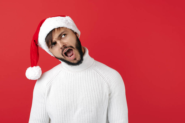 Joyful hipster man wears santa claus hat over red background. Christmas and New Year concept. - Foto, immagini