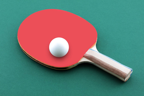 Πράσινο τραπέζι πινγκ πονγκ με μπάλα στηρίζεται σε ένα ρακέτα πινγκ-πονγκ - Φωτογραφία, εικόνα