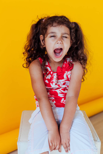 Beautiful little curly girl with braids yawns - Zdjęcie, obraz
