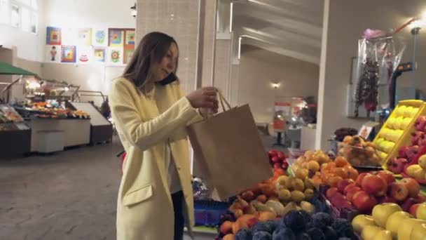 Woman in yellow coat talks on phone and puts a fresh red apples into a paper bag - Кадри, відео