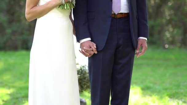 A menyasszony és a vőlegény egymás mellett állnak és fogják egymás kezét. - Felvétel, videó