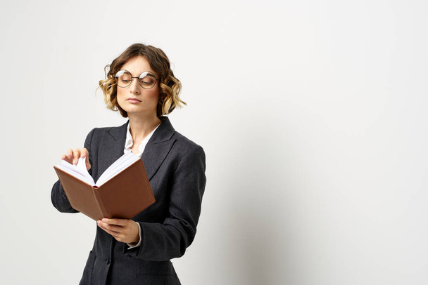 vrouw op het werk met boek in de hand licht achtergrond klassiek pak bril hoofd - Foto, afbeelding
