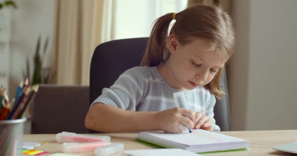 Portrait of cute concentrated little caucasian kid girl draw color pencil marker sitting at home table. Pretty preschool child coloring picture enjoy creative activity relax children distant education - Footage, Video