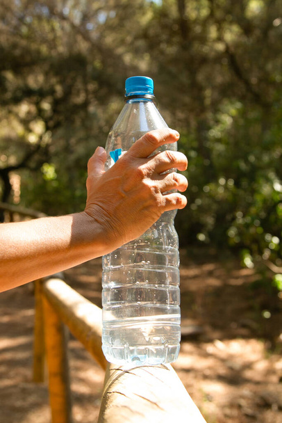 Χέρι κρατώντας ένα πλαστικό μπουκάλι με νερό στη φύση - Φωτογραφία, εικόνα