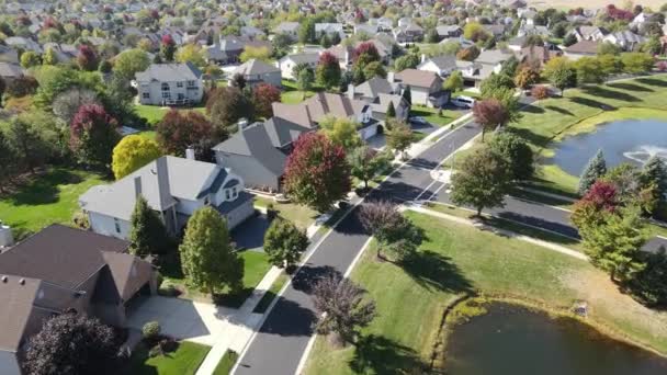 Overhead aerial view of colorful autumn trees, residential houses and yards with drainage pond along suburban street in Chicago area. Midwest USA. 4K - Footage, Video