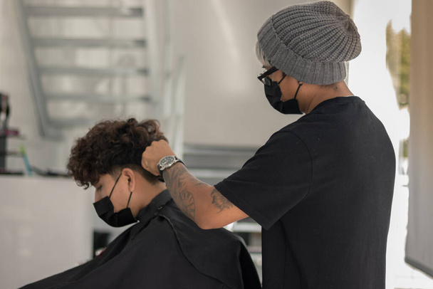 Сеанс у перукарні з молодим перукарем з маскою, що розрізає волосся хлопчика з маскою під час пандемії
 - Фото, зображення