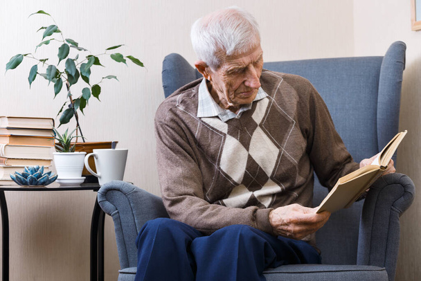 Portret seniora siedzącego w fotelu i czytającego książki. czas wolny stary ma - Zdjęcie, obraz