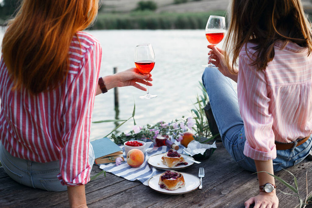 two girls enjoying picnic on a wooden pier on a shiny summer river shor - Valokuva, kuva