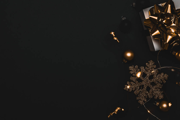 Scatola del nastro regalo. Confezione regalo bianca con nastro dorato, palline di Capodanno e ghirlanda di luci scintillanti in composizione natalizia su sfondo nero per biglietto di auguri. Natale, inverno, nuovo concetto di anno - Foto, immagini