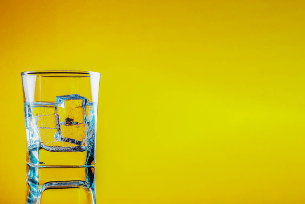 a glass of cold, clean, drinking water with ice stands on a wooden surface on an orange background. - Foto, Imagem