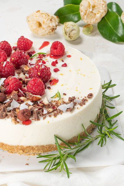 Cheesecake met frambozen, chocolade, hazelnoten en rozemarijnbladeren op keukencoutertop - Foto, afbeelding