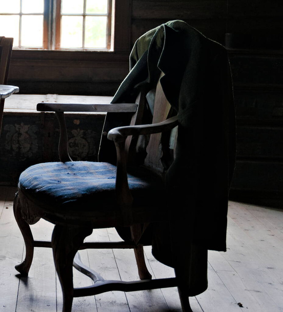 Старая куртка висит на старинном кресле с поблекшим естественным светом. - Фото, изображение